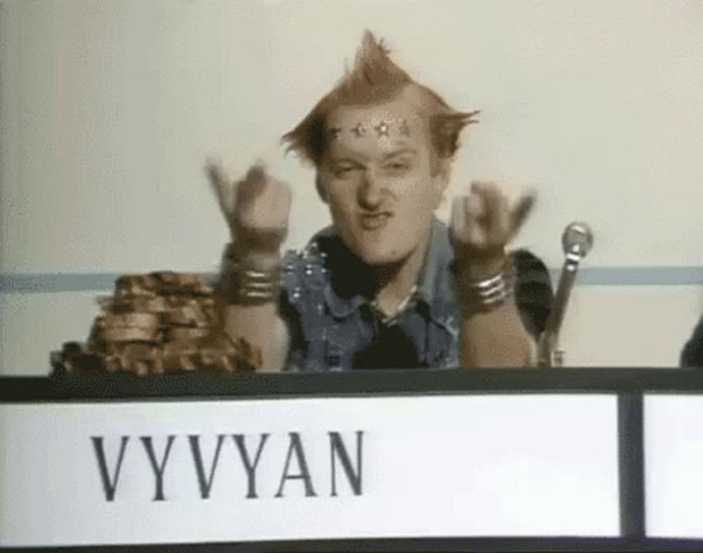 a man with a mohawk is sitting at a table with a sign that says vyvyan