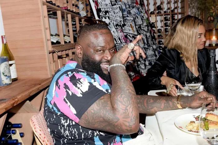 Rick Ross smiling devilishly with his pinky out. 