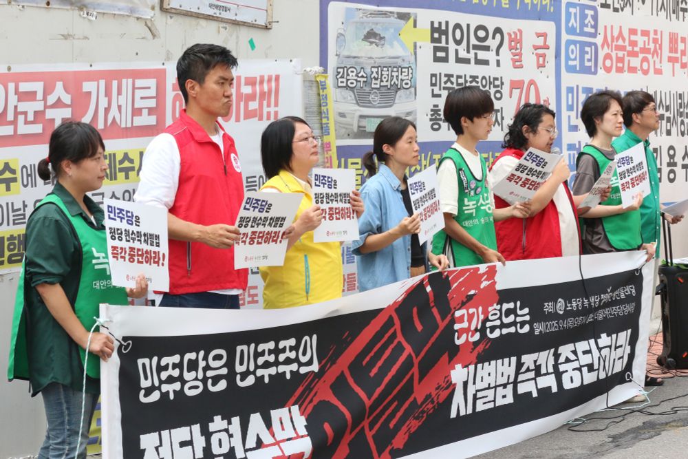 민주당 정당 현수막 차별법 관련 기자회견 사진입니다. 민주당사를 바라보며 기자회견 참여자들이 현수막 뒤에 일열로 서있습니다. 대부분 녹색당, 노동당, 정의당 조끼를 입고 있습니다. 손에는 민주당은 정당 현수막 차별법 즉각 중단하라라고 적혀있는 손피켓을 들고 있습니다. 현수막에는 민주당은 민주주의 근간 흔드는 정당현수막 차별법 즉각 중단하라, 입틀막, 주최 노동당 녹색당 정의당 은평민들레당, 일시 이천이십오년 구월 사일 목요일 오후 한시 장소 더불어민주당당사 앞이라고 적혀있습니다.

