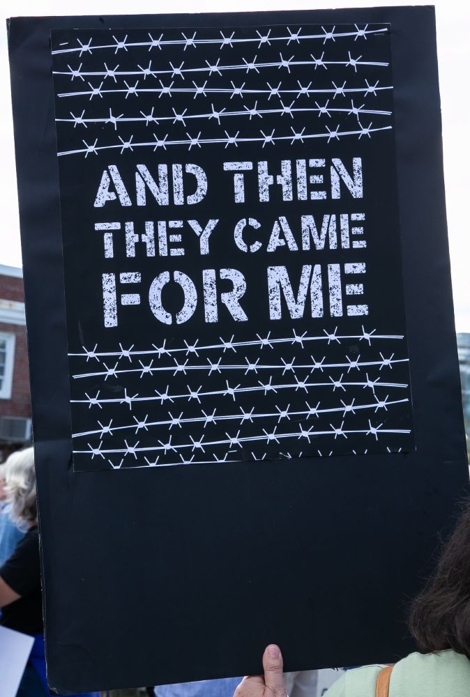 A black sign with stylized barb wire above and below the text. The text reads 
