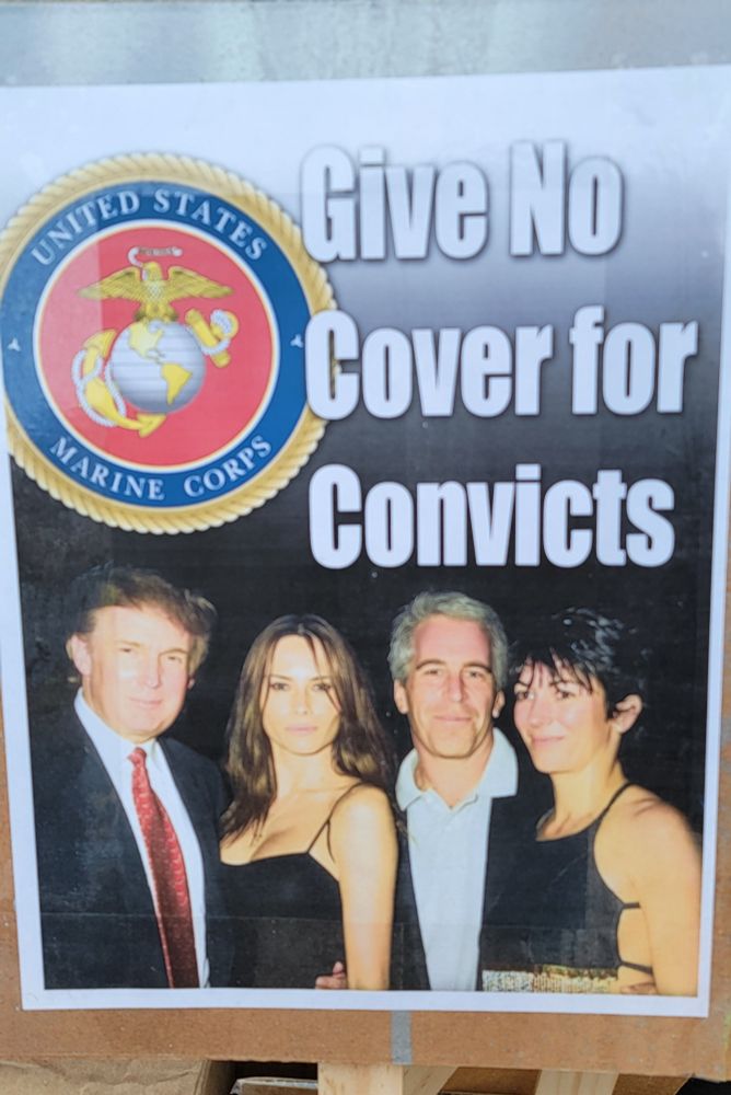 Sign with a picture of Trump and Epstein and 2 women and the marine corps seal. Text "Give no cover for convicts"
