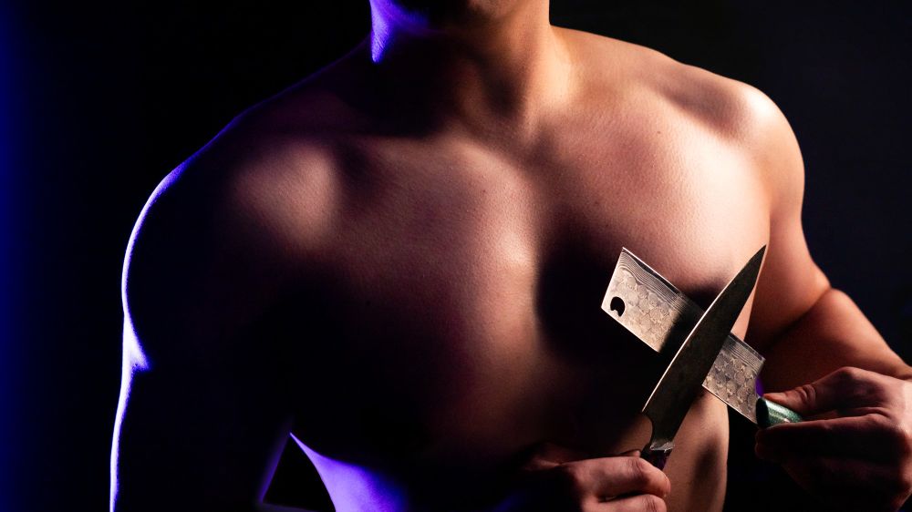 High contrast picture of a shirtless male with two knives crossed across his chest