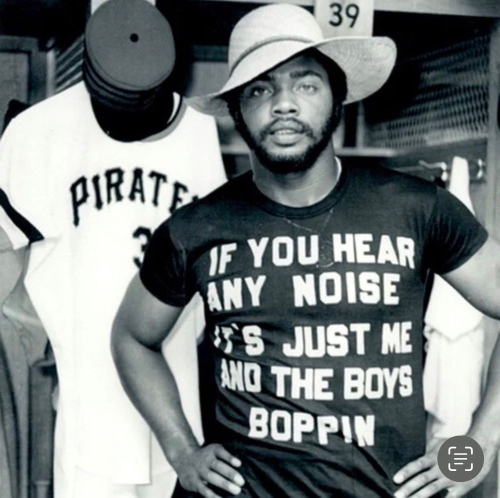 Dave Parker in a shirt he designed. It says “If you hear any noise, it’s just me and the boys boppin”. He’s also wearing what sort of looks like a cool version of a gardening hat. 