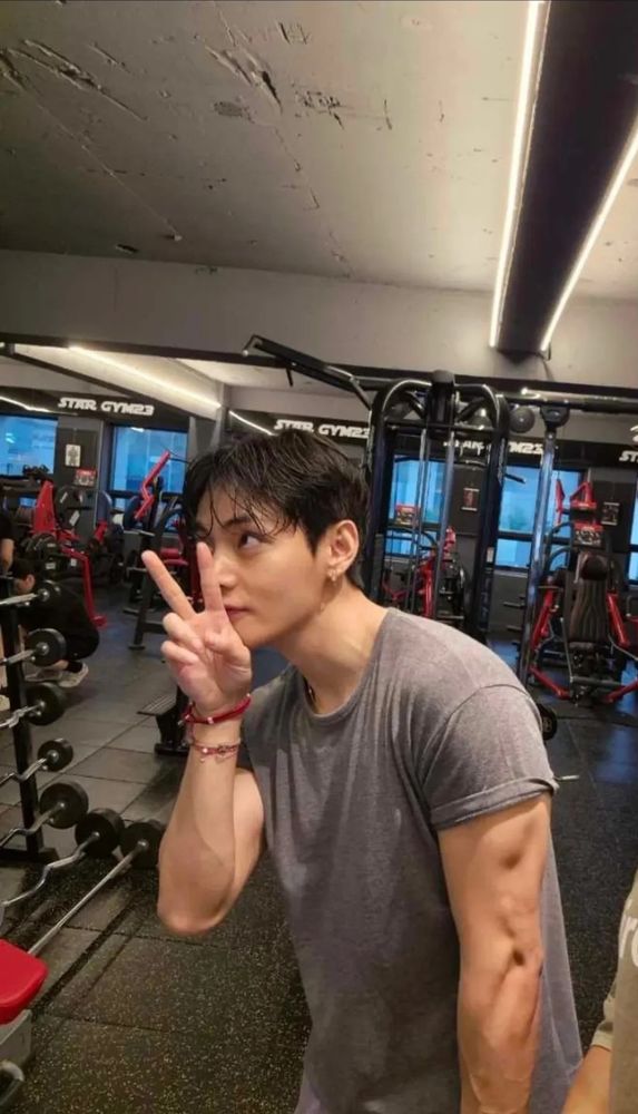 Super swole Taehyung posing for a picture in a gym. He's wearing a simple gray tshirt, the cuffs rolled up to show off his rock hard biceps and it's a problem. Not even acting cutesy and hiding behind a peace sign (as Taehyung is) negates the fact that buff Tae is here to stay.