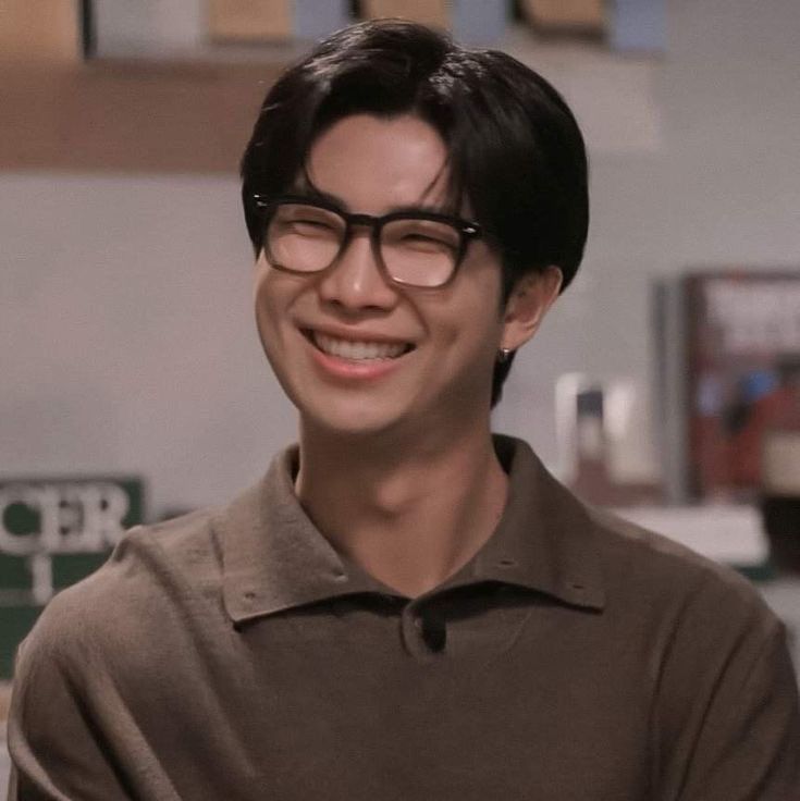 Namjoon wearing glasses and a brown polo. He's smiling so wide his eyes are happy little crescents. Dimples are popping.