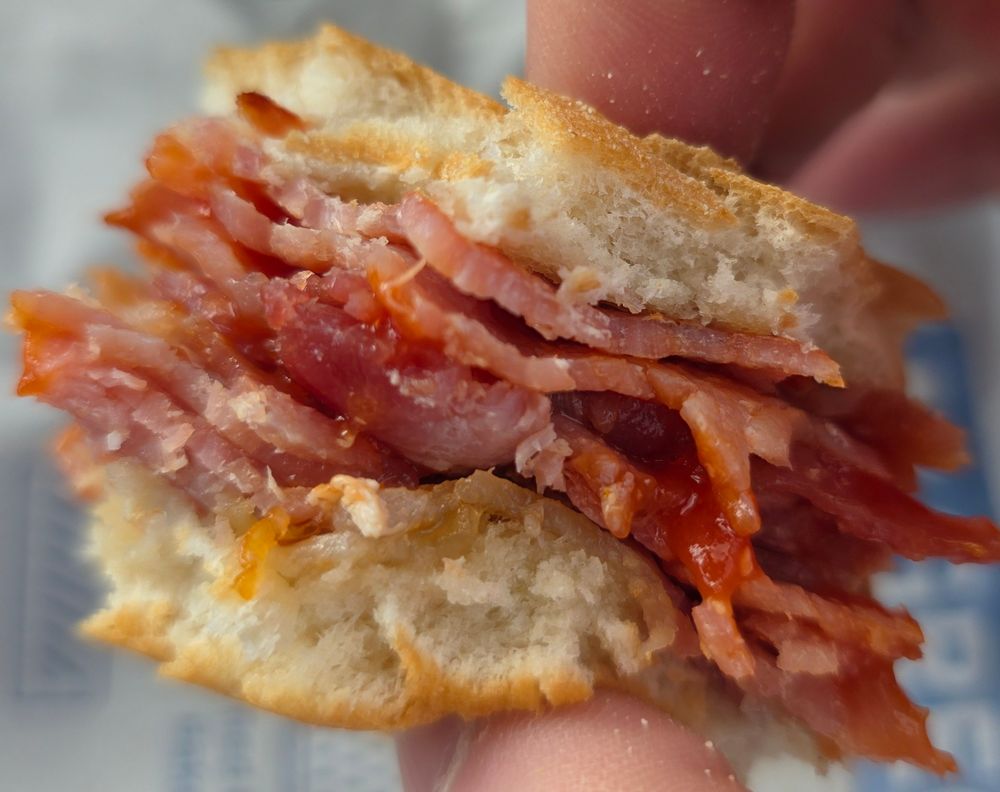 Last bite of a greggs bacon on sandwich with a lot of bacon.