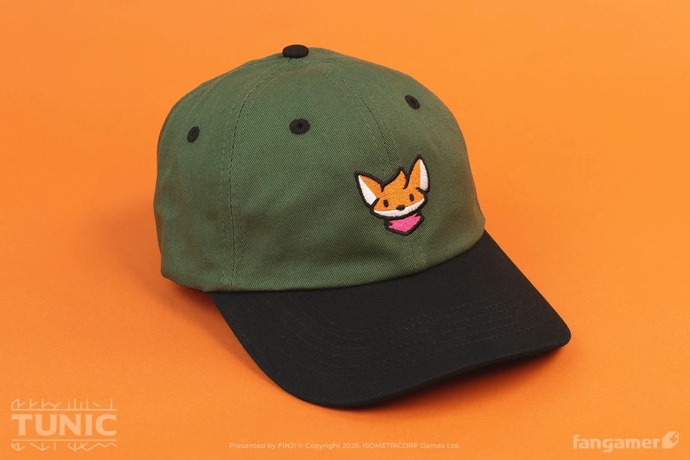 Photograph of a dark green hat with a black brim against an orange background. A cute illustration of a fox's head is embroidered on the front. 