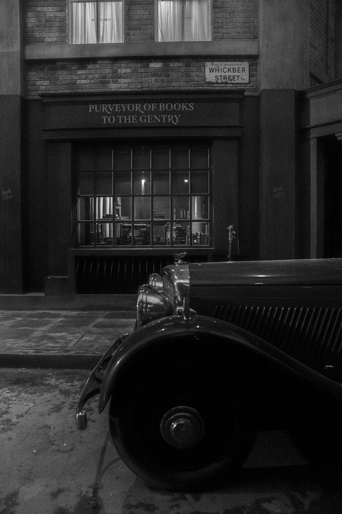A b&w bts photo of the Bentley in front of Aziraphale's bookshop
