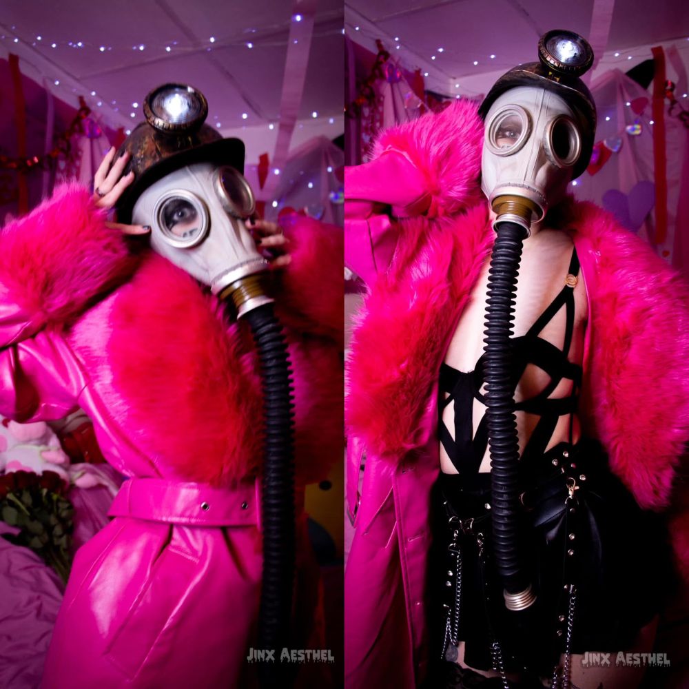 Jinx Aesthel modeling in a photoshoot inspired by the horror movie My Bloody Valentine, wearing a helmet, gas mask, pink leather coat with fur trim, and a strappy black outfit under the jacket. 