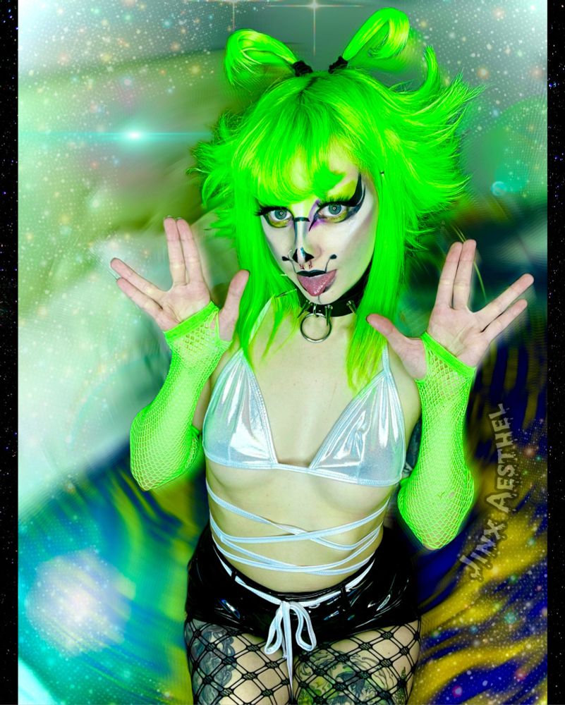 A photo of an alt girl with green hair, bright makeup, holding their hands in two Vulcan salutes