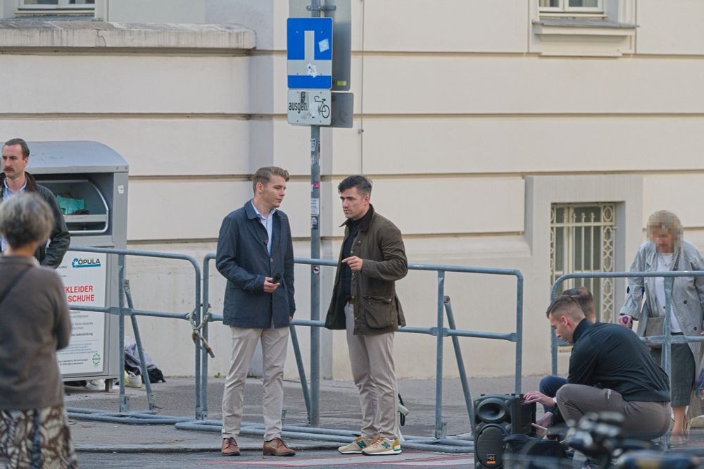 Martin Sellner und Jan Staudigl beim Vorbereiten der Rede von Staudigl in der Boltzmanngasse. Im Hintergrund Sperrgitter Richtung US-Botschaft, Staudigl hält schon ein Mikro in der Hand. 