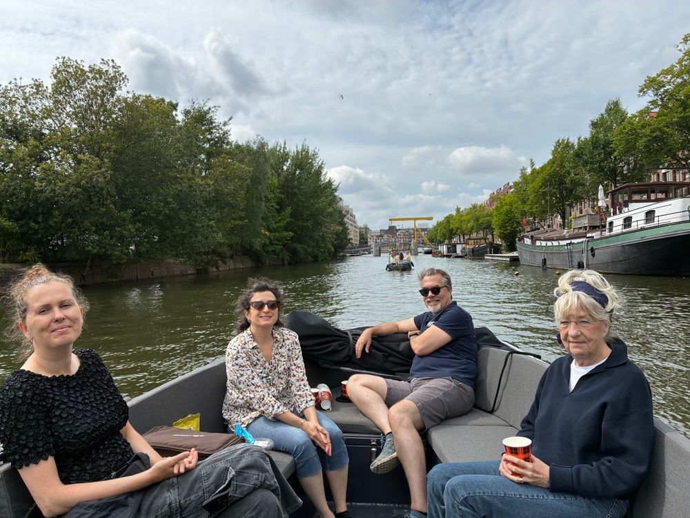 Photo of a group of friends in an open motor boat on a canal with houseboats along the side and Dutch style houses off in the distance behind 
