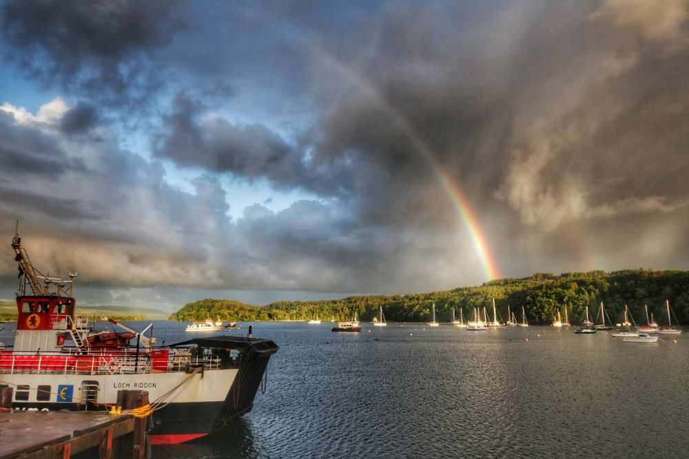 Rainbows and blue skies emerge after a heavy downpour in Tobermory Bay, Mull, Scotland