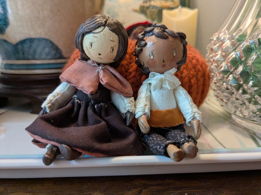 Two beautiful carved dolls. On the left is Rinsha Fana from Dungeon Meshi, on the right is girl!Kabru from Dungeon Meshi. They are in front of a crocheted pumpkin.