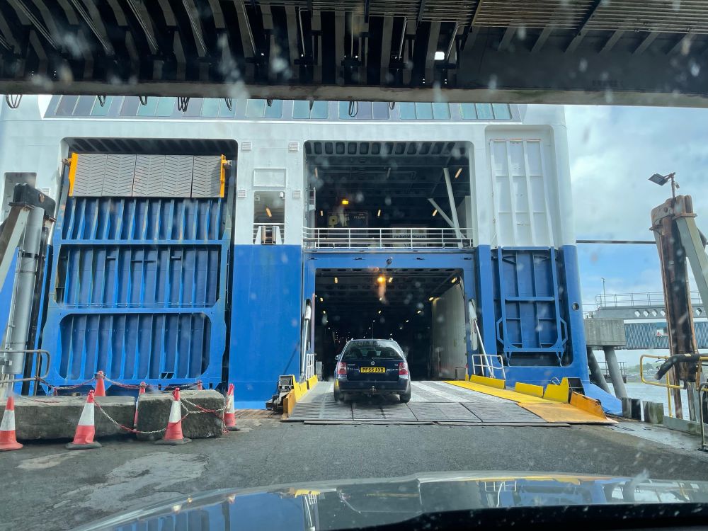 Man sieht das große Hecktor einer Fähre. Es ist geöffnet und über eine Rampe fahren Autos in die Fähre.