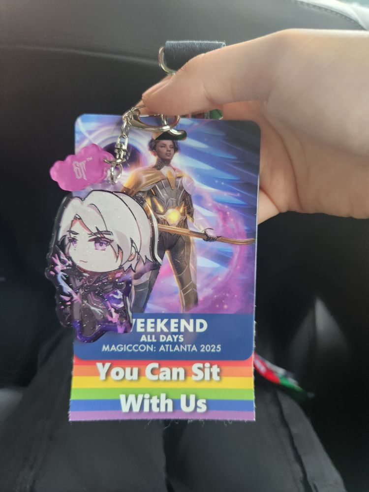 A MagicCon Atlanta weekend badge with Haliya on it. An acrylic keychain of Alpharael is attached.