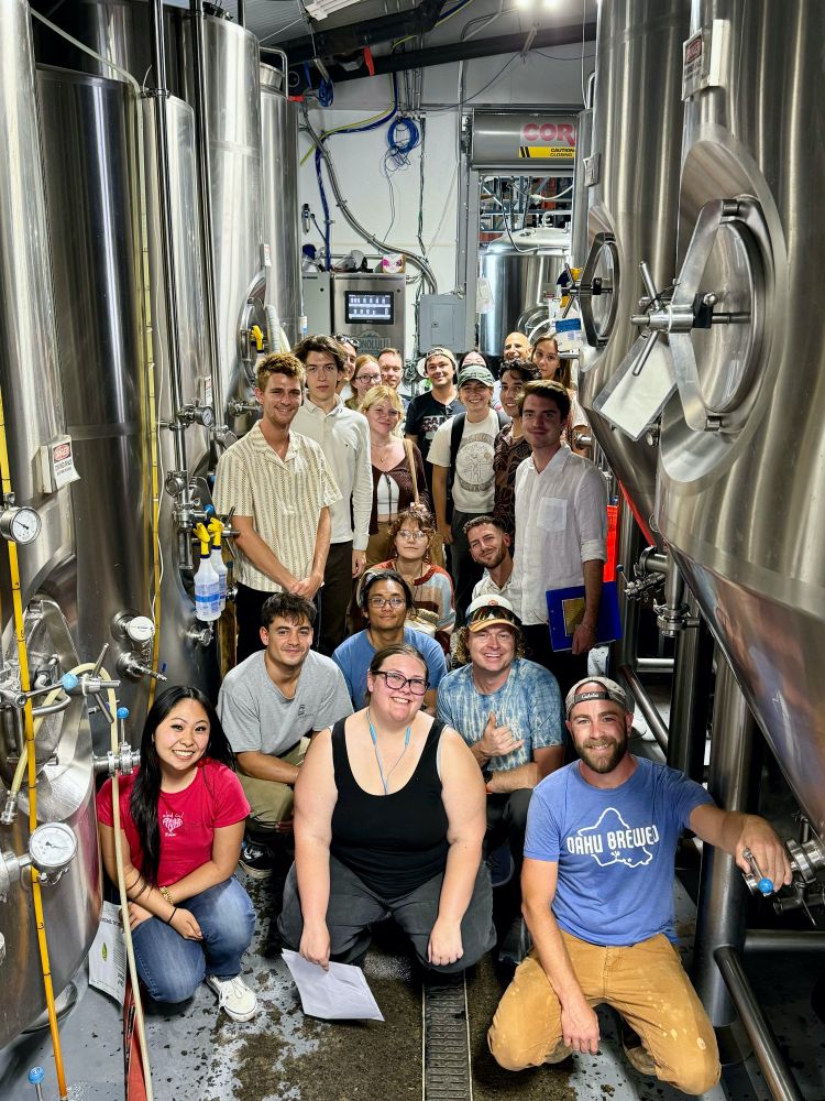 Mycology class posing in front of fermenters in a brewery.