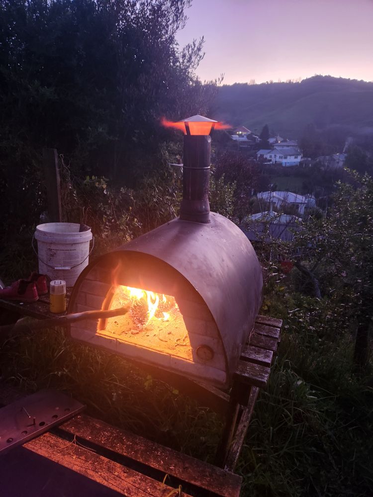 An old maximus pizza oven, door open. A blazing fire inside blasts up and out the chimney 