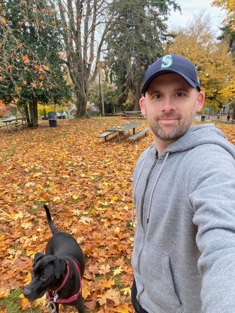 me and Toby (a black dog) in a park with the ground covered in orange, yellow, and brown leaves