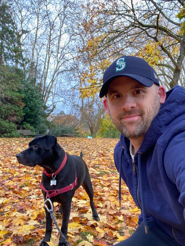 me and Toby (a black dog) at the park with a bunch of leaves on the ground and some trees in the background