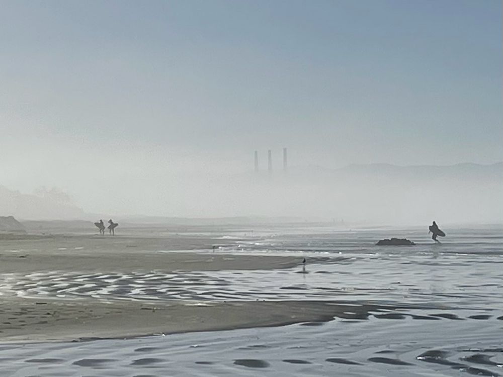 Foggy beach with three surfers in the background