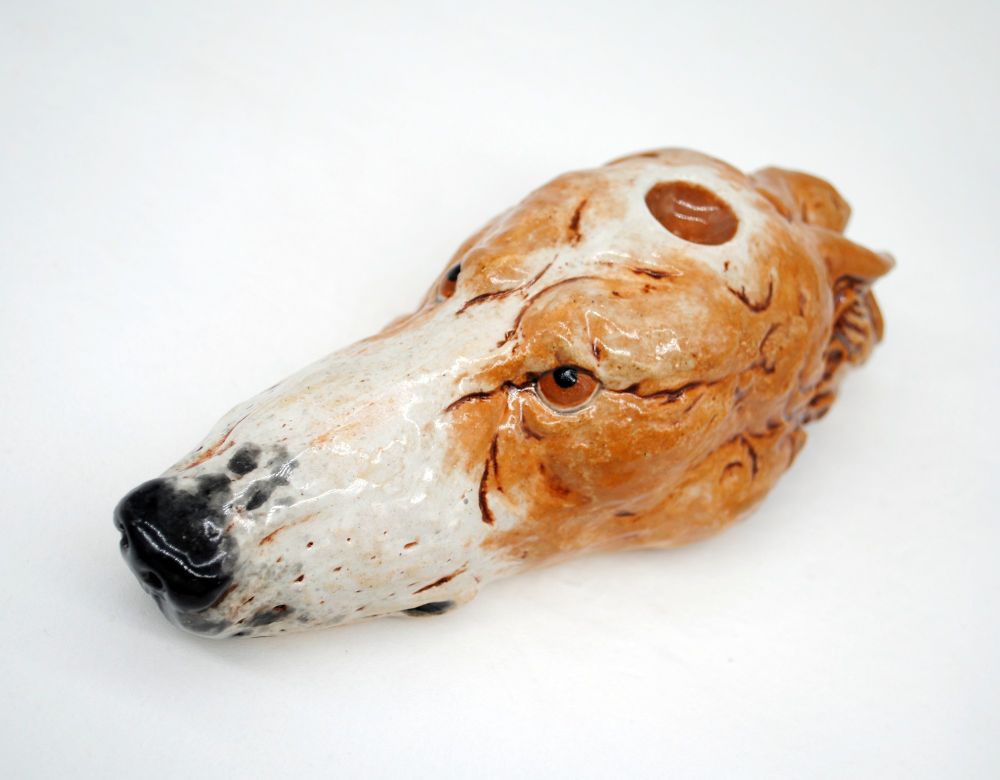 photo of a ceramic pipe in the shape of a tan and white borzoi head on a white background. photo is taken from a high angle to show the eyes of the dog and the bowl atop the head. 