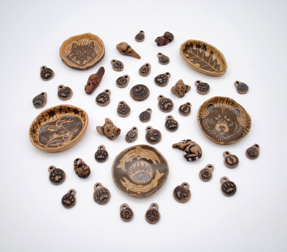 photo featuring pottery pieces and a variety of pendants in the shape of animals like beaver, raccoon, opossum, squirrel, and animal track pendants