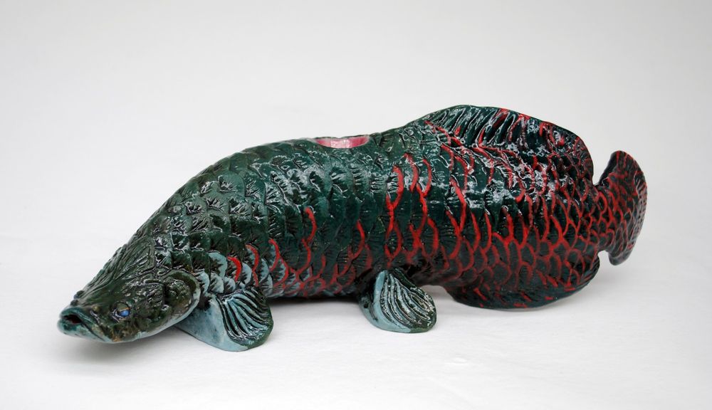 photo of a ceramic pipe with a white background, the pipe is in the shape of a arapaima fish with green, teal and deep red coloring