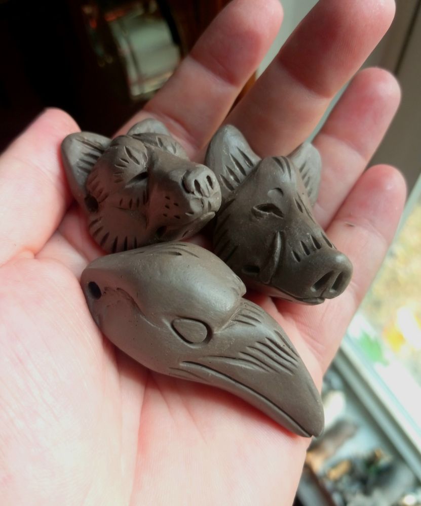 Photo of three wet clay animal head shaped pendants in the palm of a hand, a wolf, boar, and raven