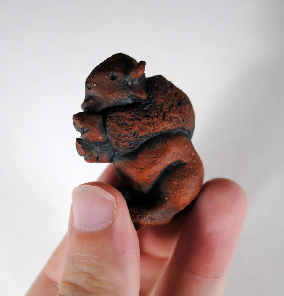 image of a red clay bison pendant being held in fingers, white background
