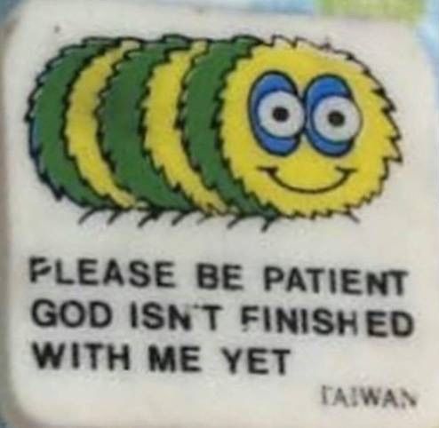 A patch from a thrift store that reads "PLEASE BE PATIENT GOD ISNT FINISHED WITH ME YET" featuring a drawing of a deeply deranged-looking caterpillar with deep blue shadows under its eyes