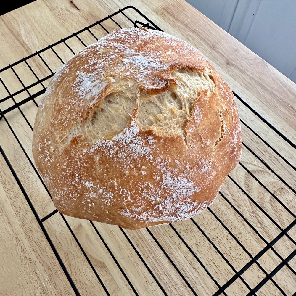 A round loaf of bread sits atop a cooling rack.