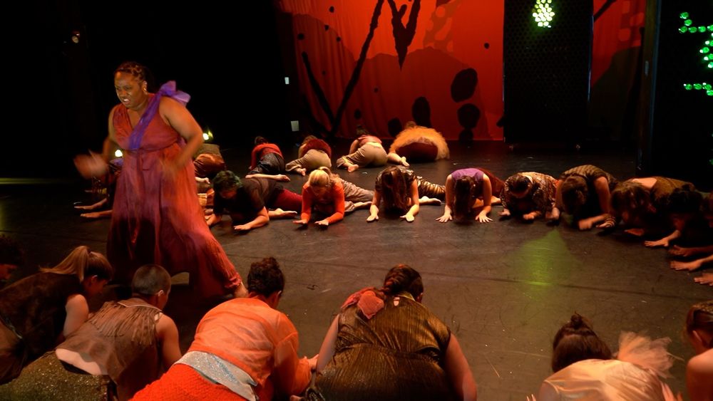 A dance performance showing woman dancing while many other women form a circle around her on the ground.
