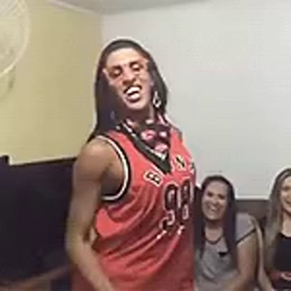 a woman in a red basketball jersey is dancing in front of a group of people .