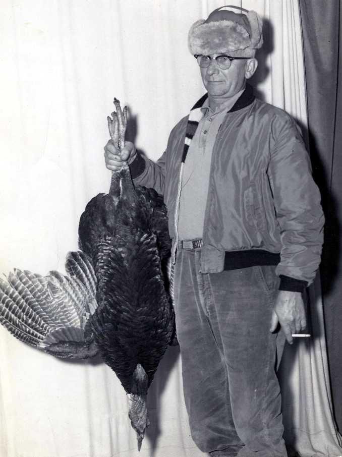 my grandpa holding a cigarette and a turkey in front of some drapes