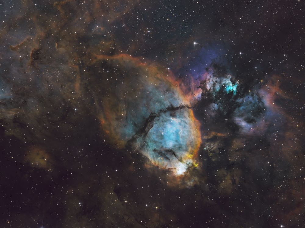 The fish head, like the heart nebula, is outlined in oranges with a blue core. It has a few dark features going through the core, giving the appearance of gills and fishy facial features. Above the fish head is an area that is a blast of color, filled with violets, purples, and teals. 