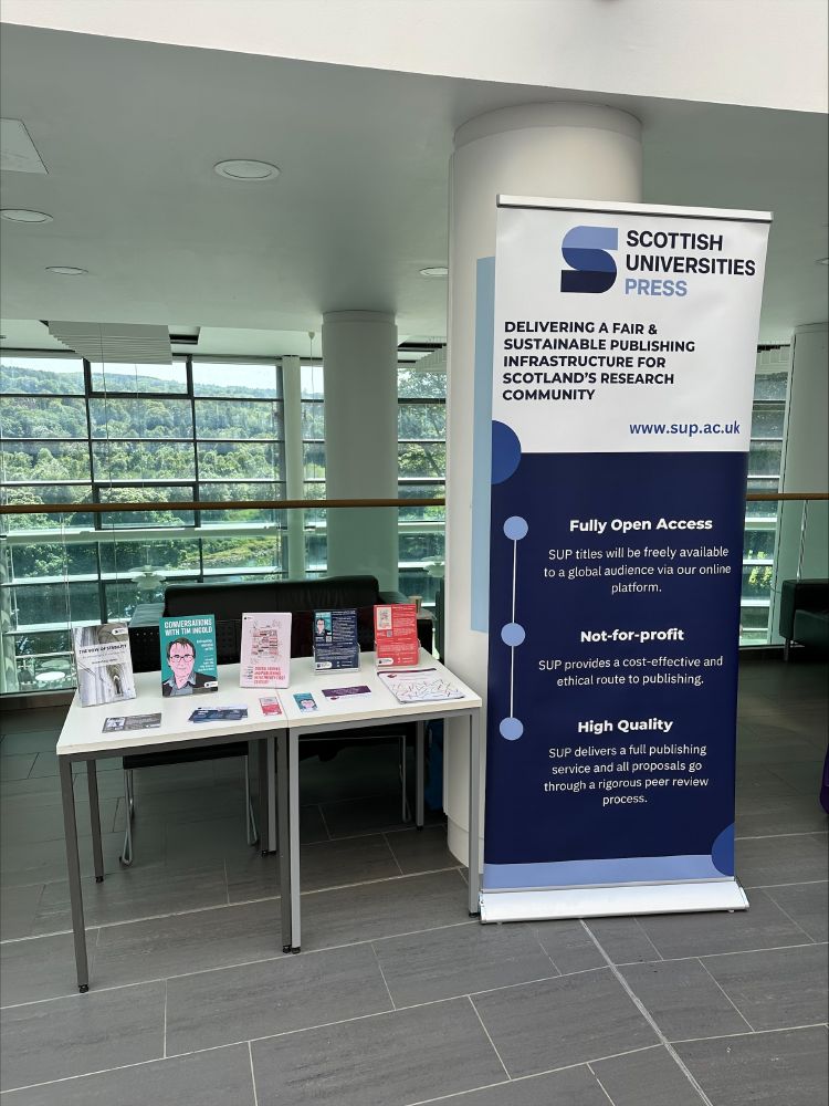 A photograph of a table displaying Scottish University Press (SUP) books and flyers next to an SUP pop-banner at the Robert Gordon University 
