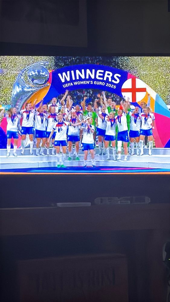Women lifting a trophy on football pitch on a thanks 