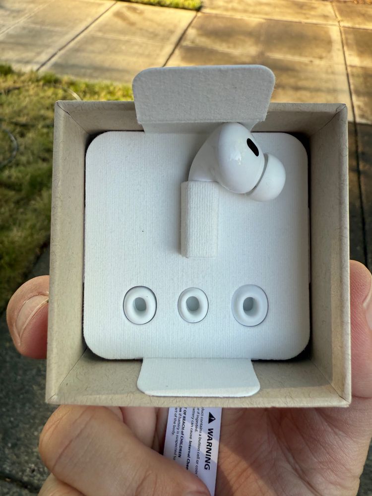 A photograph of a cardboard box containing a single left AirPod.