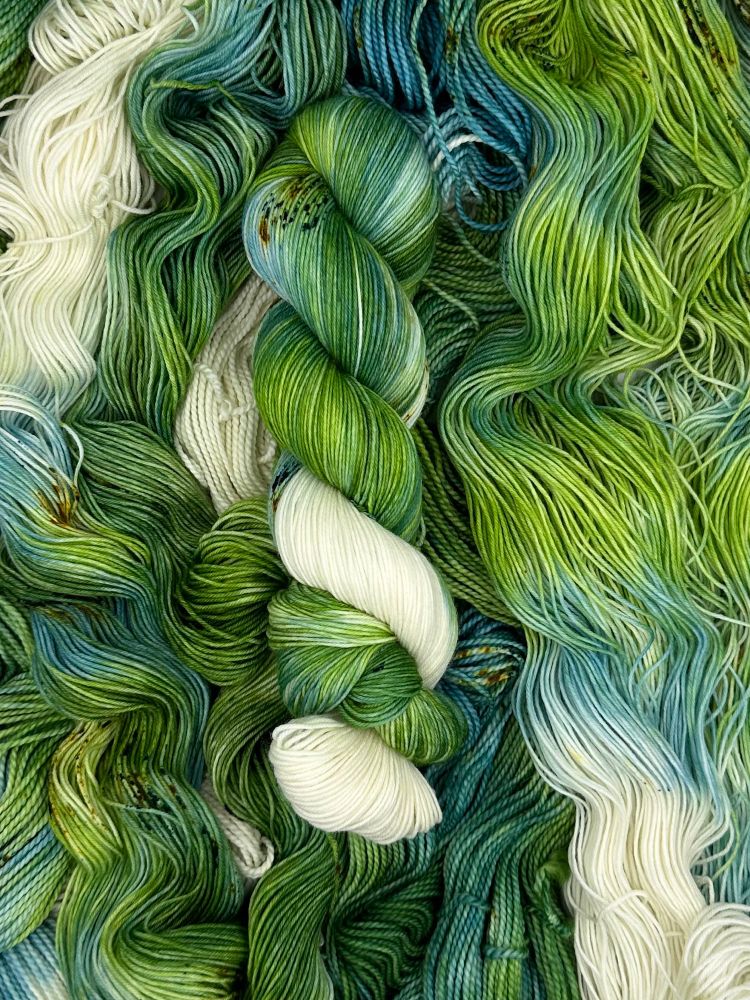 A green, blue and white twisted hank on a bed of untwisted hanks 