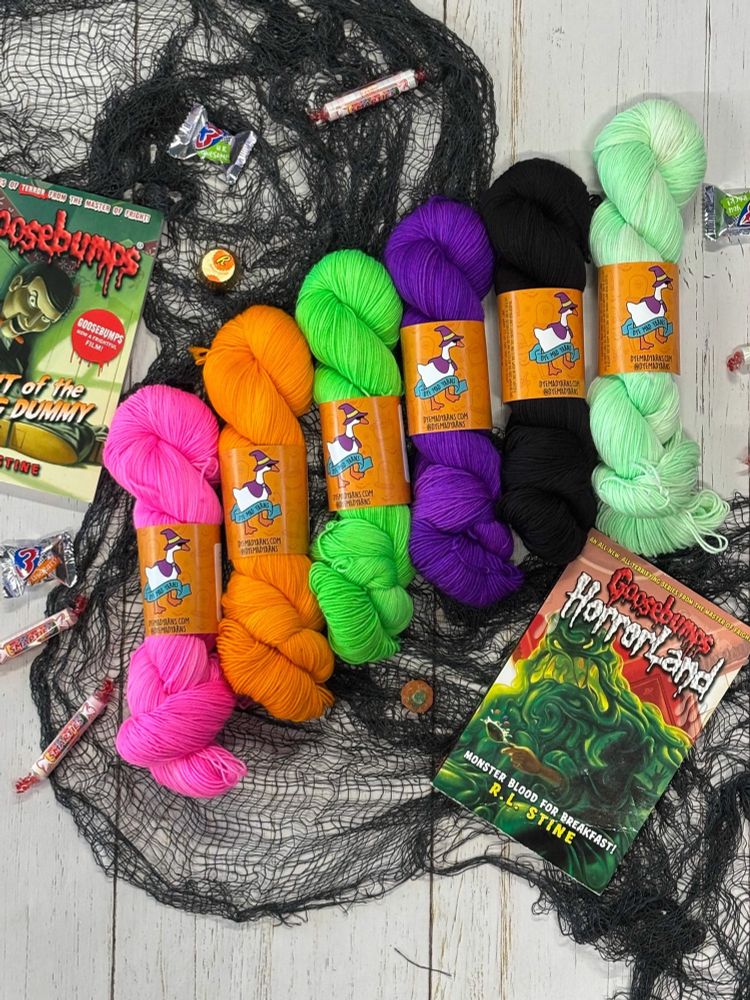 Our Halloween collection of yarns with twisted hanks in neon pink, bright orange, neon green, neon purple, black and a ghostly green. Product photos have Goosebumps books, netting, and Halloween candy. 