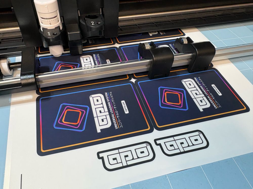 A plotter device cutting out TapTo stickers to be applied to NFC cards.