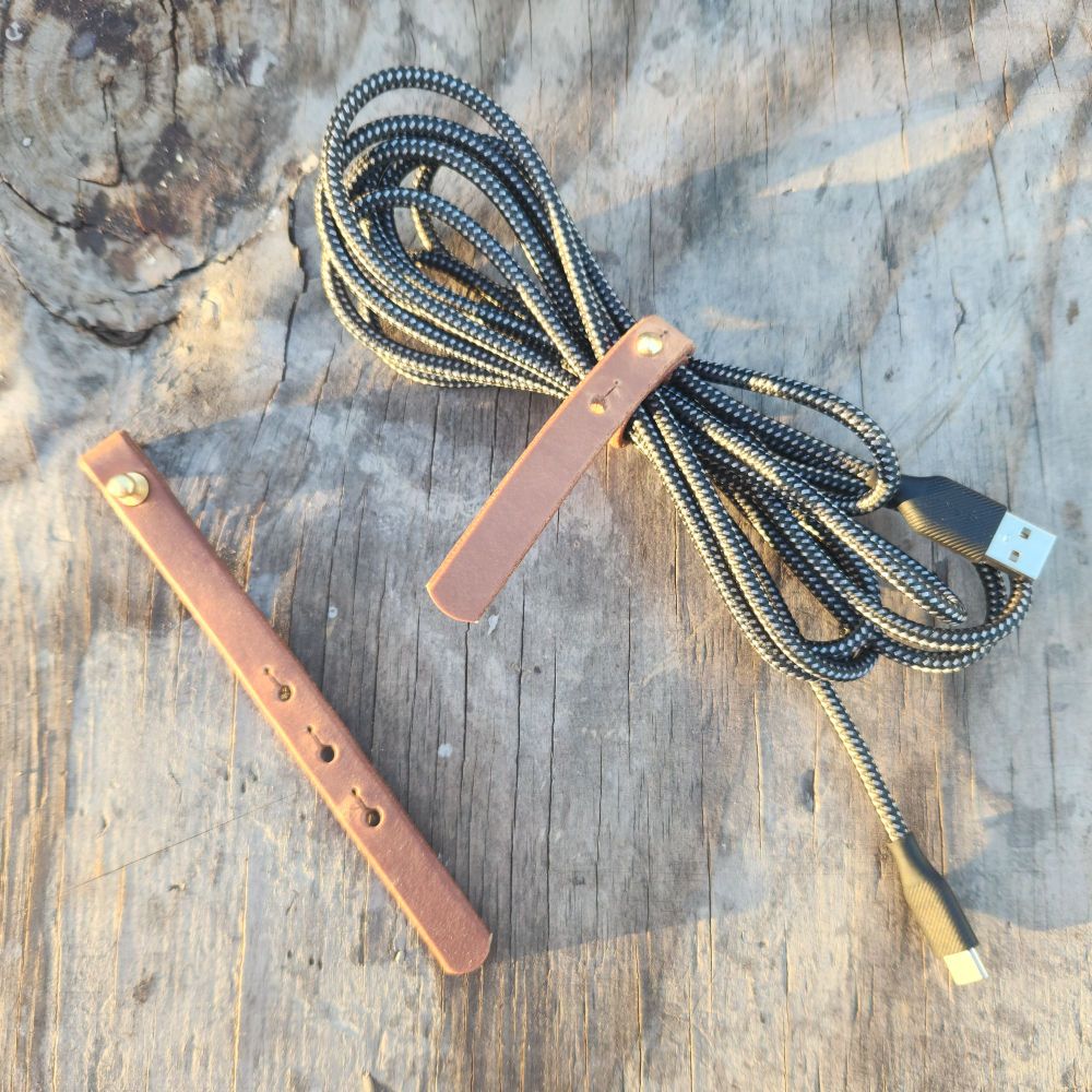 Two brown leather keepers for charging cables are seen here, one holding a cable together and the other open and flat on the table.