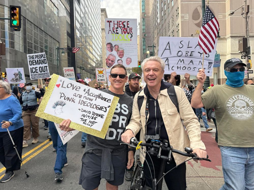 Image from No Kings march in NYC 10/18/25 with David Byrne posted next to a guy whose sign reads: “Love & Acceptance are now punk ideologies— David Byrne”