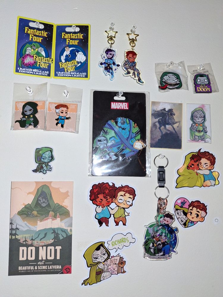 A random assortment of enamel pins, acrylic keychains, and stickers featuring Reed Richards & Doctor Doom, several are of Doom alone
