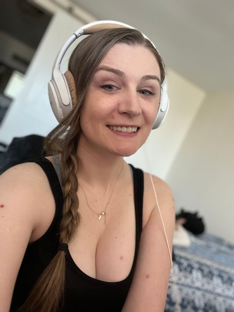 Selfie of Crev wearing a black tank top and white headphones her hair is in a side braid 