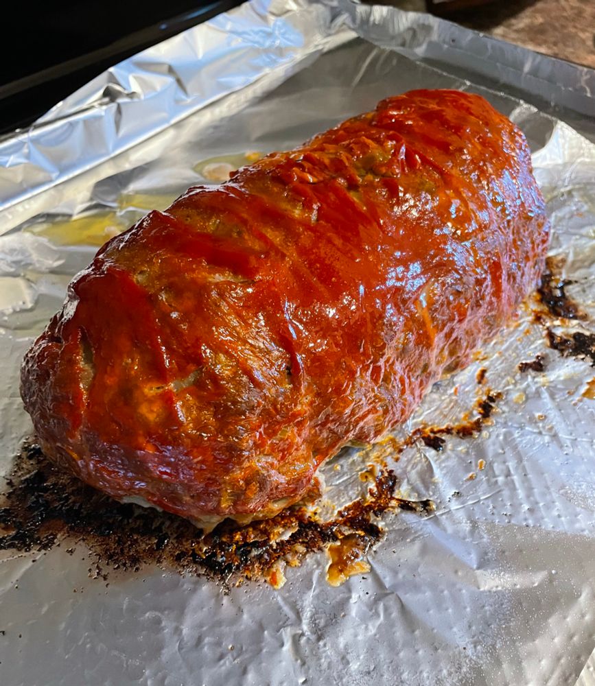 a meatloaf. slightly pill shaped, on a baking sheet instead of in a loaf pan. it is glazed with ketchup and mustard mixed together. 