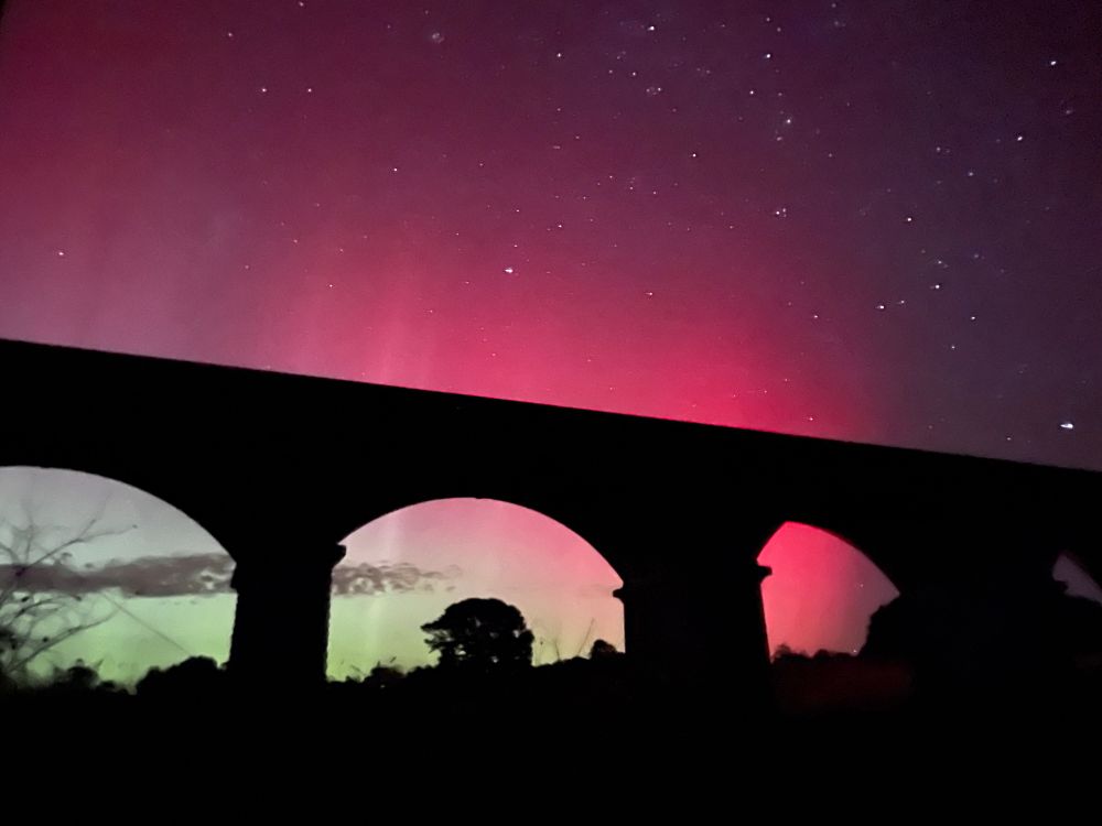 Aurora Australis glowing green, red, and pink, as seen through an old bluestone viaduct 