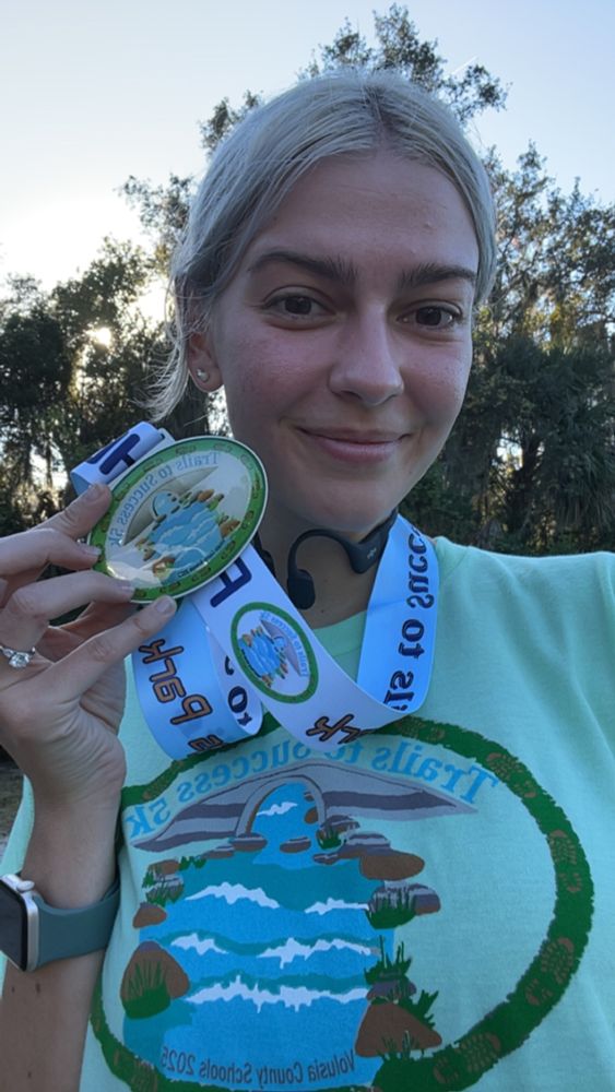 Me smiling holding a medal for a 5k race
