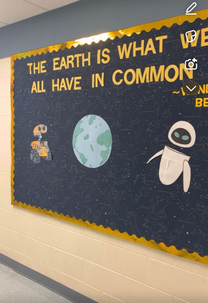Hallway bulletin board. The quote says “the Earth is what we all have in common - Wendell berry”. The background is space constellations and in the middle are Wall-e and Eve with the earth in the middle 